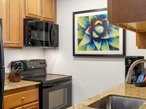 A kitchen with wooden cabinets, a microwave, a stove, and a sink. - Club Wyndham Desert Rose Resort (Las Vegas)