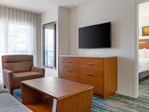 A hotel room with a flat-screen TV mounted on the wall, a wooden dresser, a single armchair, and a small table. - Club Wyndham Desert Rose Resort (Las Vegas)
