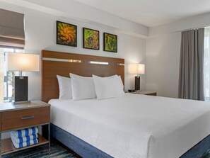 A hotel room with a large bed, two bedside tables, a nightstand, a lamp, a window with curtains, and three framed pictures on the wall. - Club Wyndham Desert Rose Resort (Las Vegas)