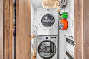A compact laundry room with two washing machines, a drying rack, and a detergent bottle. - The Owl House | A Playful 70s Tahoe Donner Escape (Truckee)