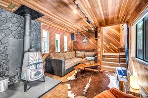 A cozy cabin interior with a stone fireplace, wooden walls, a sofa, and a cowhide rug. - The Owl House | A Playful 70s Tahoe Donner Escape (Truckee)