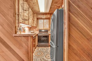 A compact kitchen with wooden walls, a refrigerator, a stove, and a patterned floor. - The Owl House | A Playful 70s Tahoe Donner Escape (Truckee)