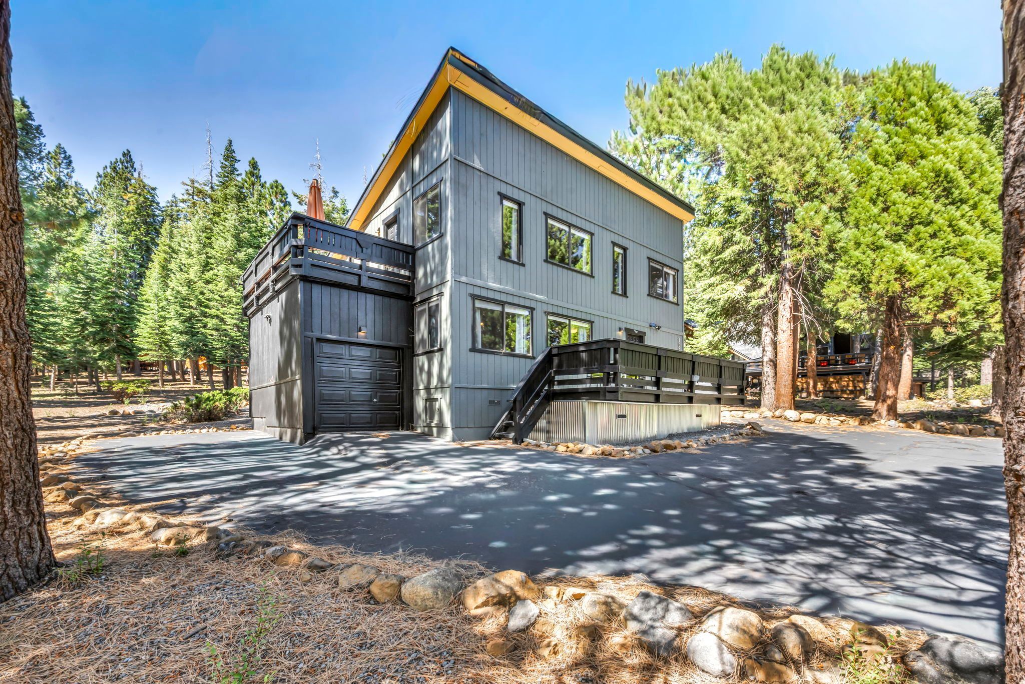 Un bâtiment à deux étages avec un garage, entouré d’arbres et bordé d’un chemin en pierre.