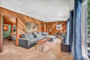 Ein modernes Wohnzimmer mit einer Eckcouch, einem Couchtisch und einem großen Fenster mit Vorhängen.