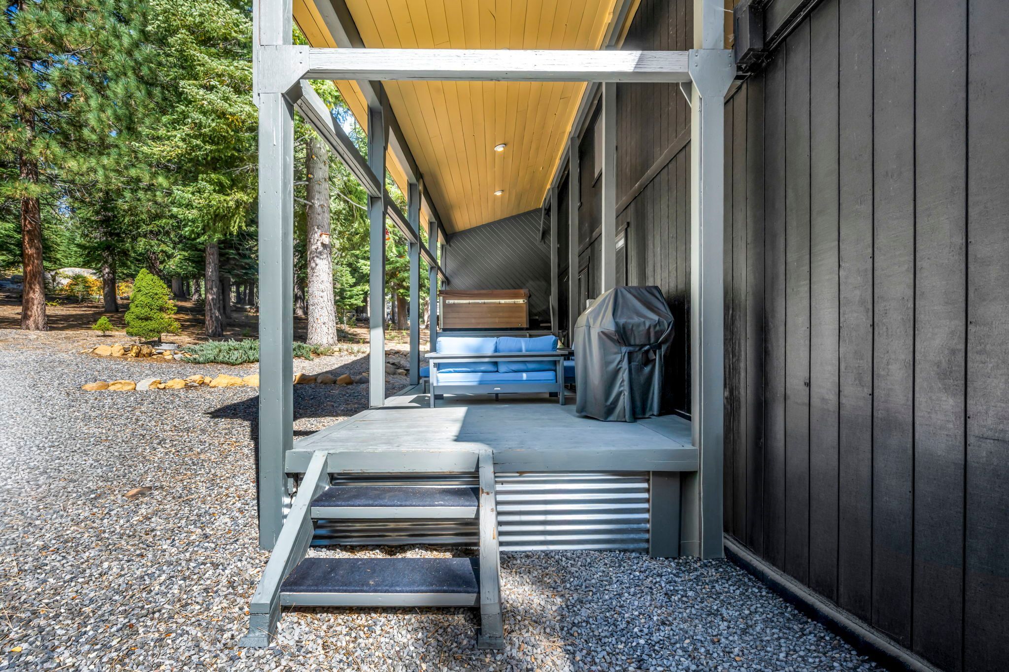 A covered outdoor seating area with a bench and a grill, surrounded by trees.