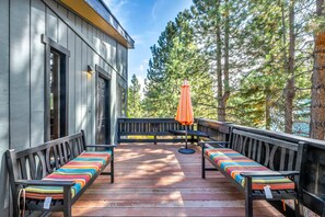 An outdoor deck with two benches, an umbrella, and a view of trees. - The Owl House | A Playful 70s Tahoe Donner Escape (Truckee)