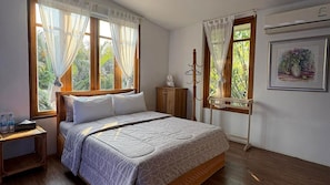 Un dormitorio con cama, mesita de noche, armario de madera y ventana con cortinas.