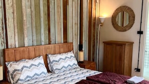 A bedroom with a wooden headboard, two pillows, a bedside lamp, a mirror, and a wooden cabinet.