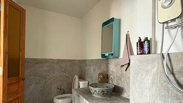 Un baño con inodoro, bidé y lavamanos con un recipiente decorativo.