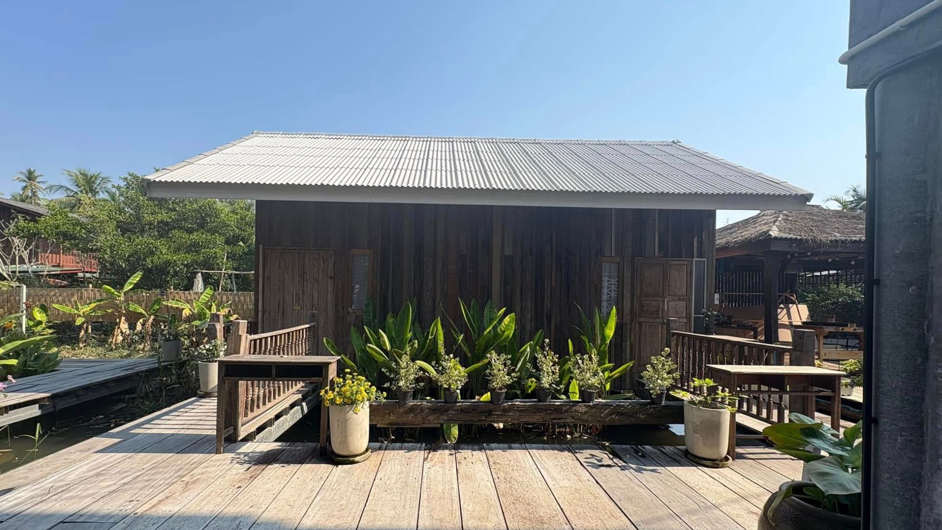 Une terrasse en bois dotée d’un espace salon abrité, entourée de plantes en pot et d’une clôture en bois.