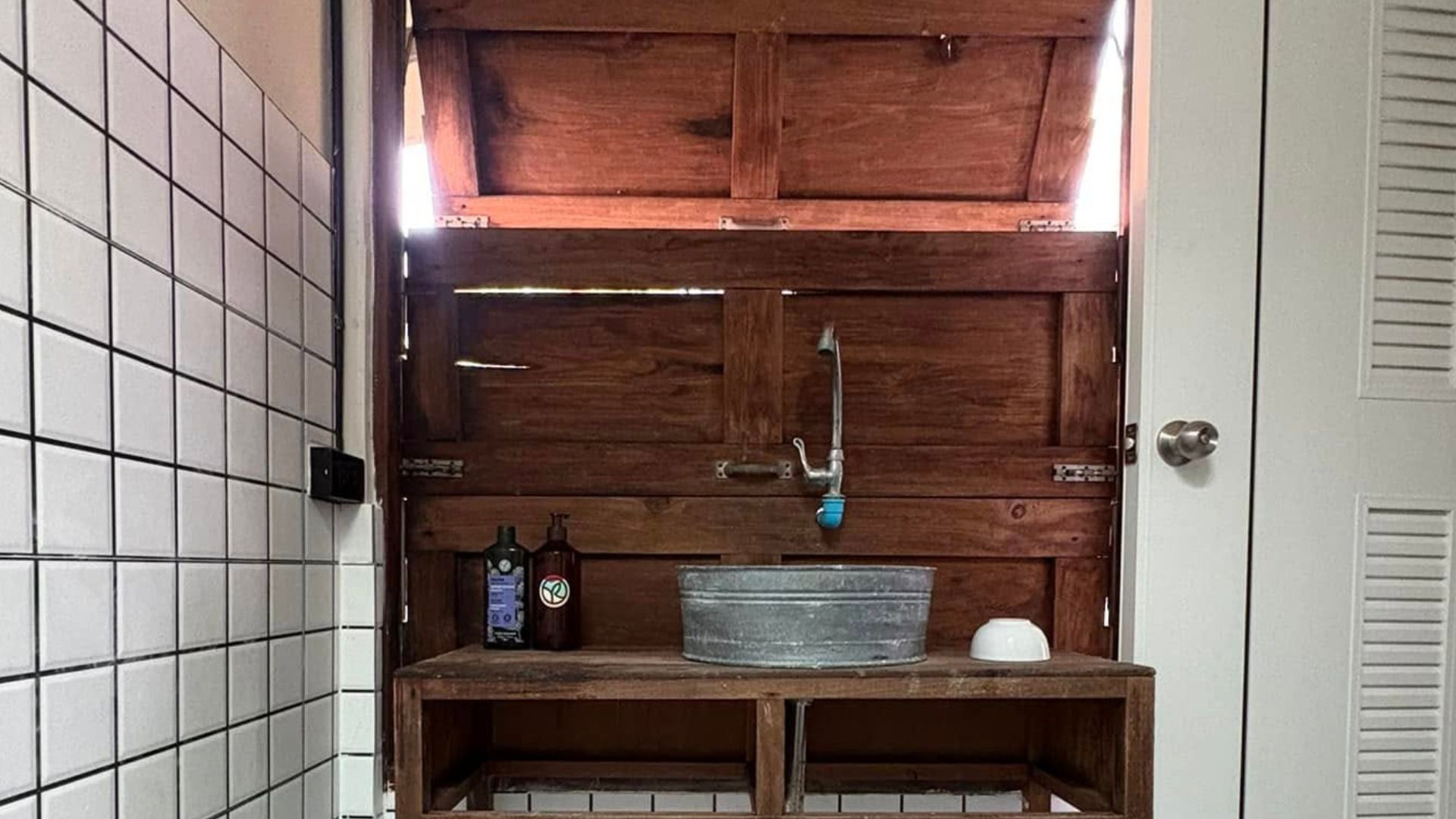 Un baño con tocador de madera, lavamanos metálico y dos botellas sobre la encimera.