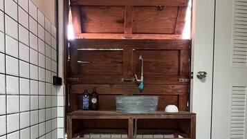 Un baño con tocador de madera, lavamanos metálico y dos botellas sobre la encimera.
