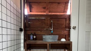 Un baño con tocador de madera, lavamanos metálico y dos botellas sobre la encimera.