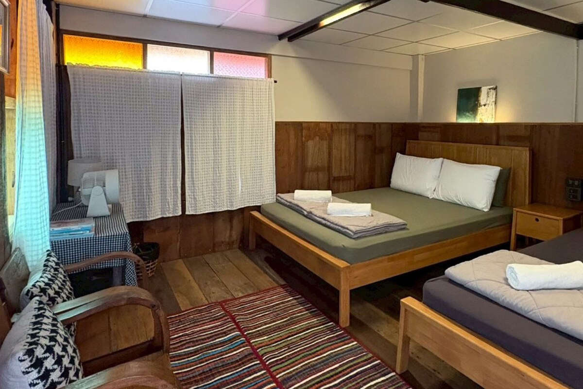 Una habitación con cama, un banco, un escritorio, una silla y una ventana con cortinas.