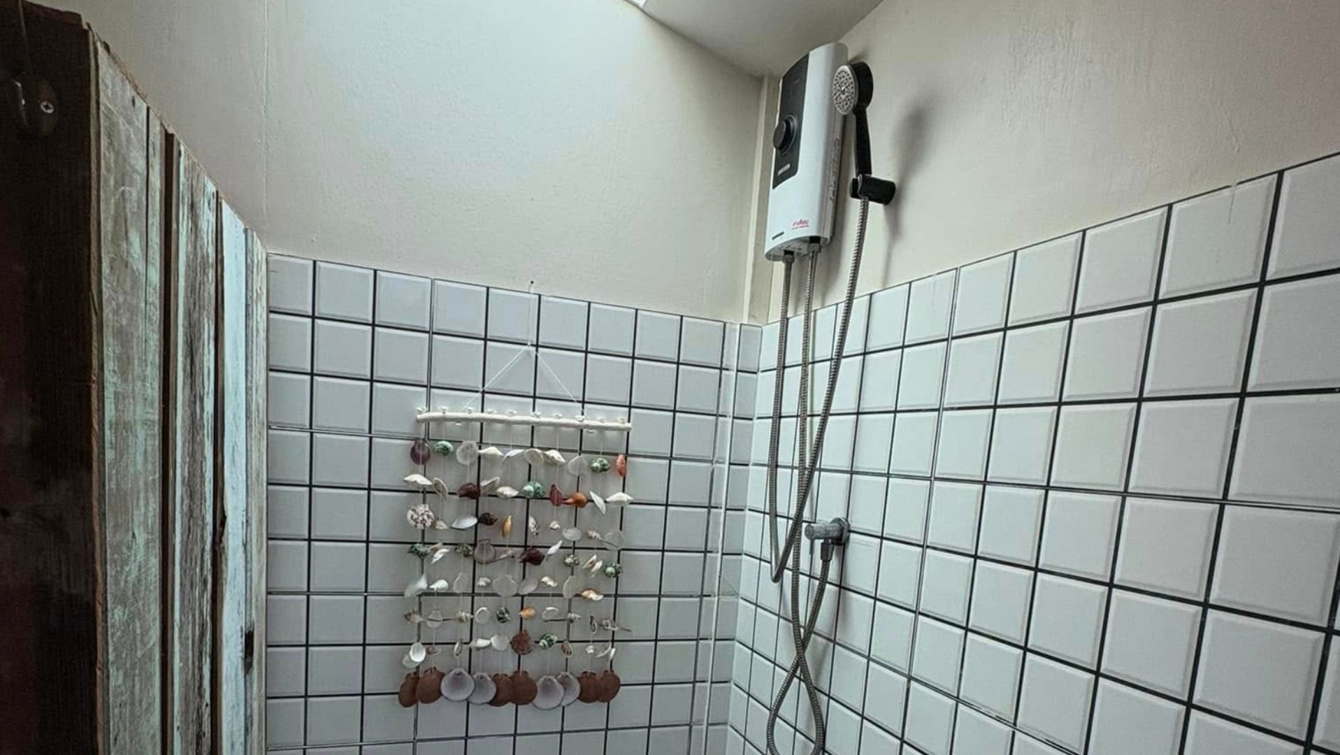 Une salle de bain avec des murs carrelés de carreaux blancs, un porte-serviettes suspendu avec divers articles de toilette et une douchette à main.