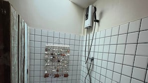 A bathroom with white tiled walls, a hanging rack with various toiletries, and a handheld showerhead.
