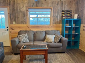 A living room with a sofa, coffee table, and a blue shelving unit against a wooden wall.