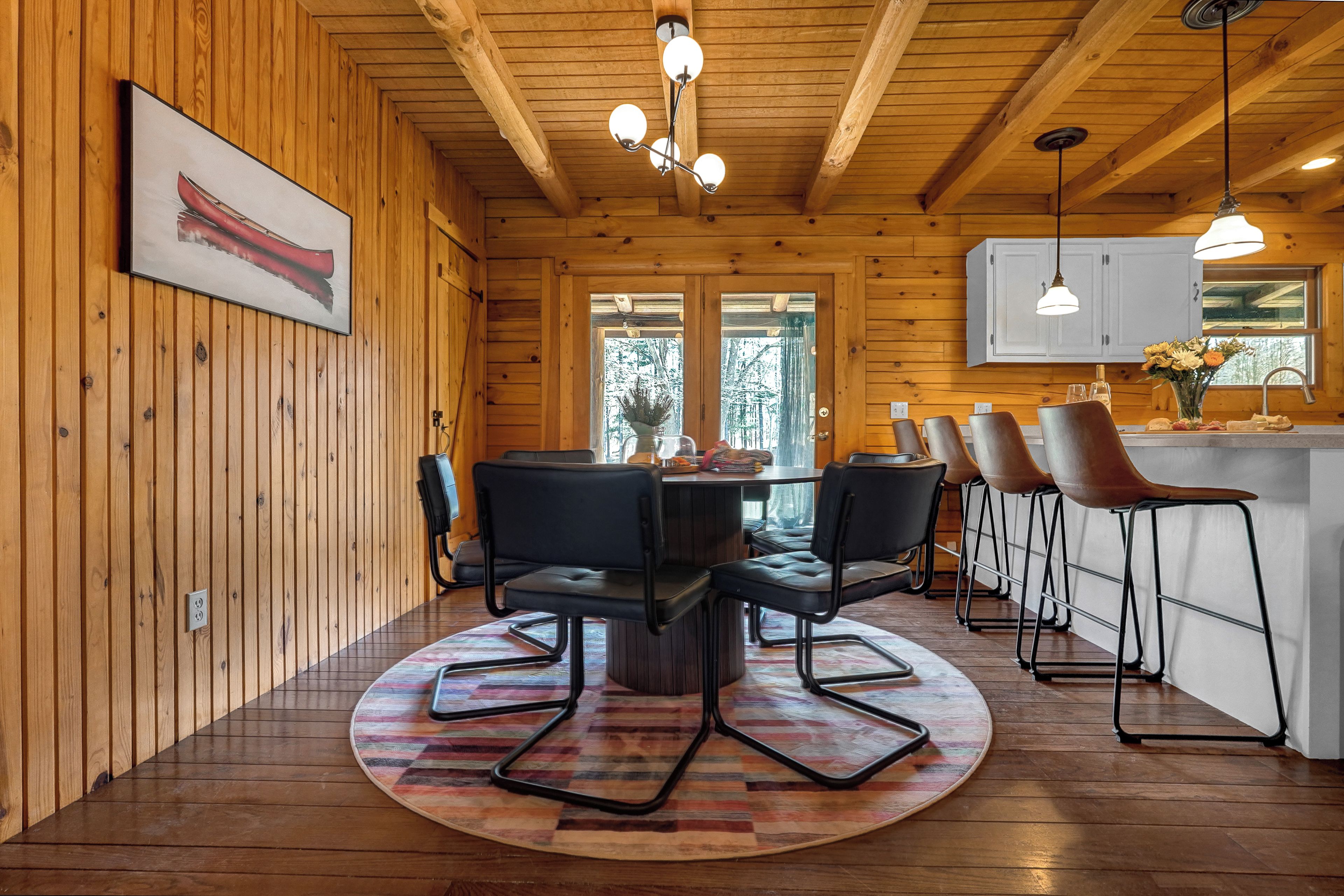 A wooden interior with a round dining table, black chairs, and a kitchen area with bar stools.