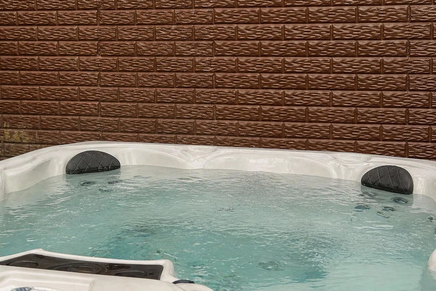 Un bain à remous doté de deux espaces assise, installé devant un mur en briques.