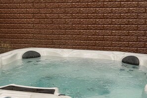A hot tub with two seating areas, set against a brick wall backdrop.