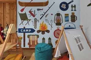 Une pièce dont un mur est décoré d’une fresque représentant du matériel de camping et une tente sur laquelle est écrit le mot « CAMP ».