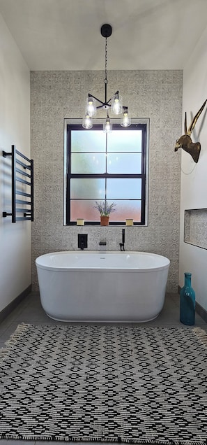 Un bagno moderno con una vasca da bagno indipendente, una parete decorata, una grande finestra e un lampadario a parete decorativo.