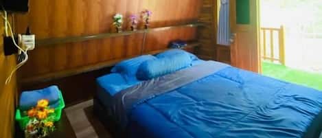Un dormitorio de cabaña de madera con cama, almohadas, una mesita de noche y una ventana.