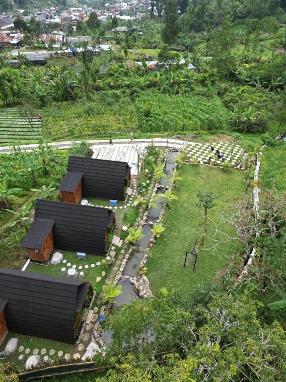 A rural setting with several wooden cabins arranged around a central path, surrounded by lush greenery and a small pond.