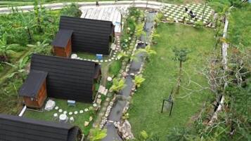 A rural setting with several wooden cabins arranged around a central path, surrounded by lush greenery and a small pond.
