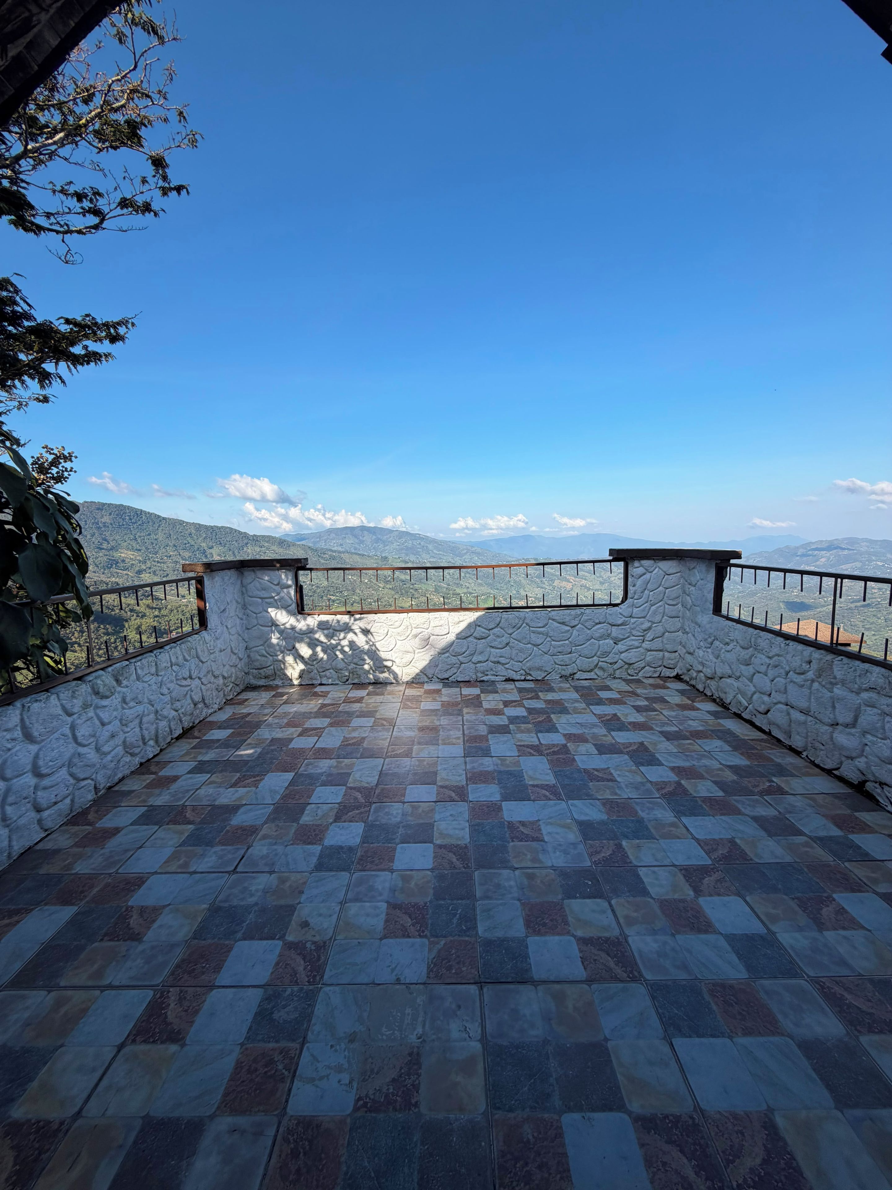 Eine Terrasse mit Steinwänden, Fliesenboden und Metallgeländer mit Blick auf eine gebirgige Landschaft.