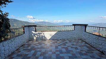 Eine Terrasse mit Steinwänden, Fliesenboden und Metallgeländer mit Blick auf eine gebirgige Landschaft.