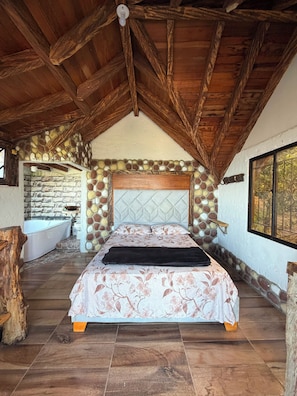 A bedroom with a stone wall, a wooden ceiling, a large bed, and a view of the outdoors. - El Colibrí Cabin in Cocorná: Incredible View (Cocorná)