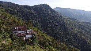 Paesaggio montuoso con un piccolo edificio dotato di tetto rosso e pareti bianche, circondato da vegetazione lussureggiante.