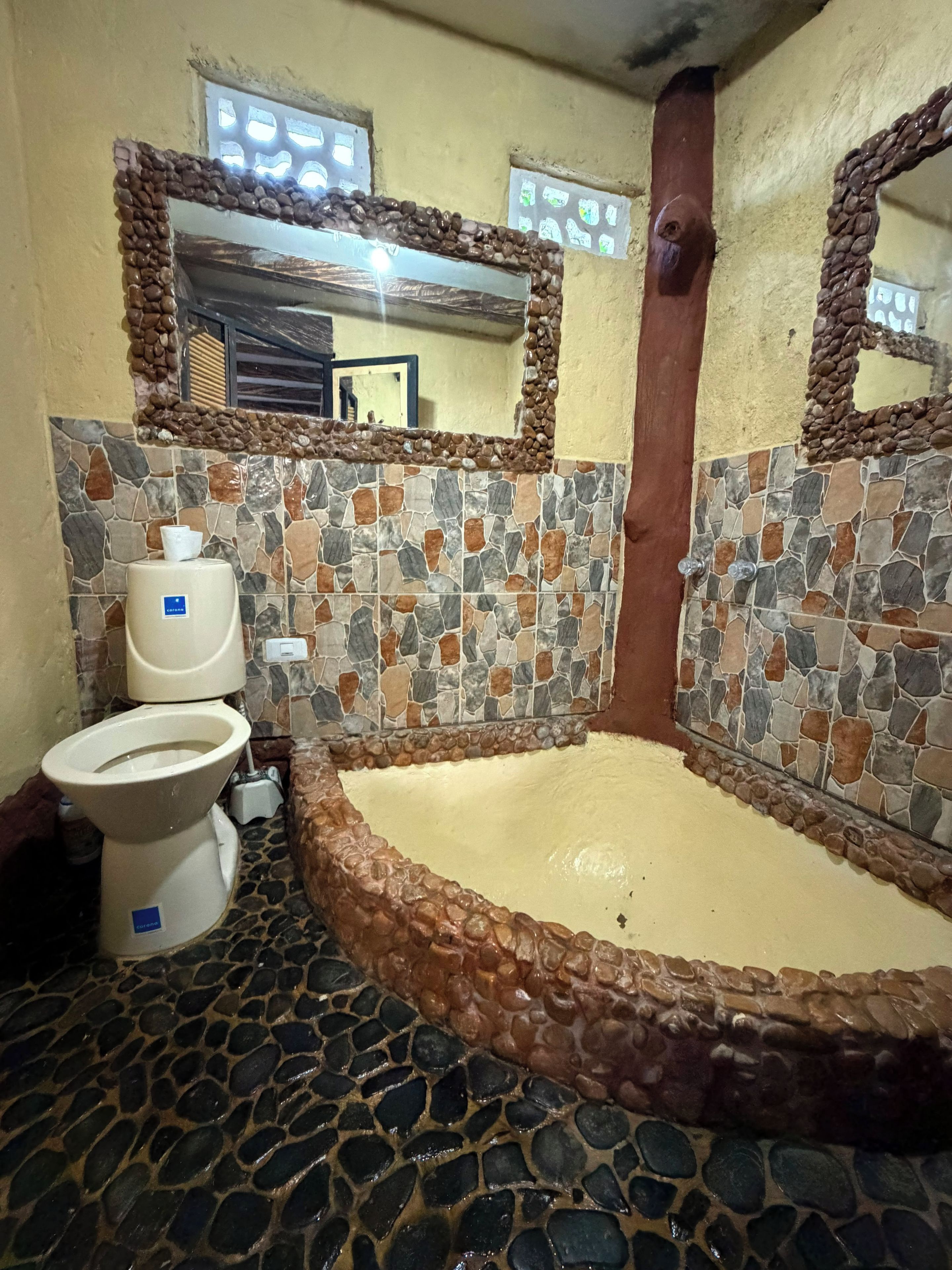 Ein Badezimmer mit Stein-Mosaikboden, einer Toilette und einer Badewanne.
