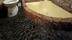 Casa de banho com parede em mosaico de pedra, sanita e banheira.