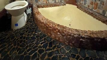 Ein Badezimmer mit Stein-Mosaikboden, einer Toilette und einer Badewanne.