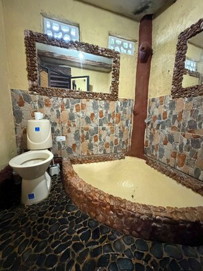 A bathroom with a stone mosaic wall, a toilet, and a bathtub. - El Colibrí Cabin in Cocorná: Incredible View (Cocorná)