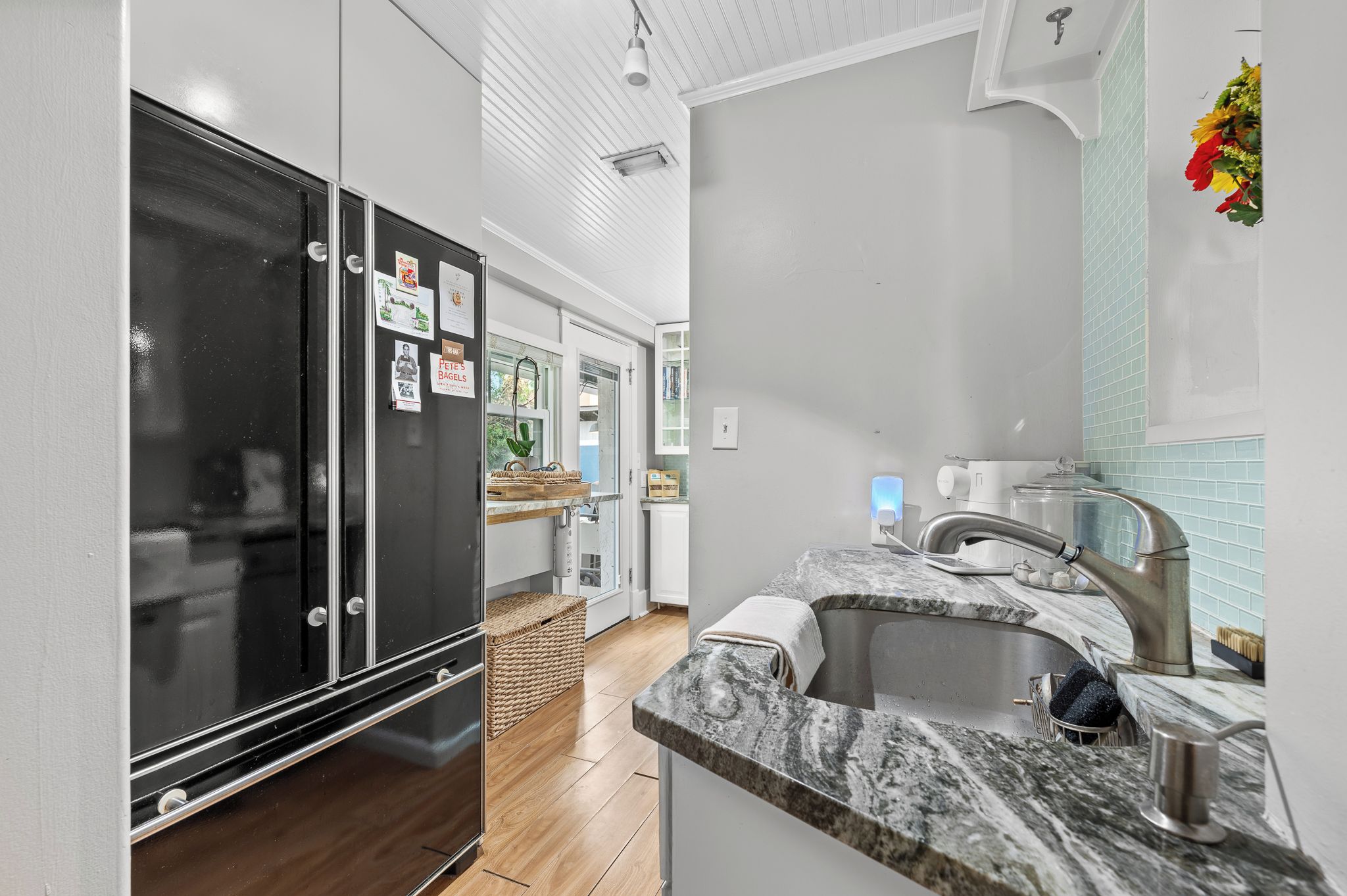 A modern kitchen with a black refrigerator, a marble countertop, and a sink.