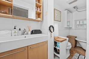 A bathroom with a white sink, mirror, and a wooden vanity. There is a toilet with a wicker basket beside it, and a shower area with a white tub. - StayHaus - The Meridian Flat (St. Petersburg)