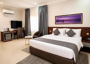 Una habitación de hotel con una cama grande, un escritorio con televisor y un cuadro en la pared.