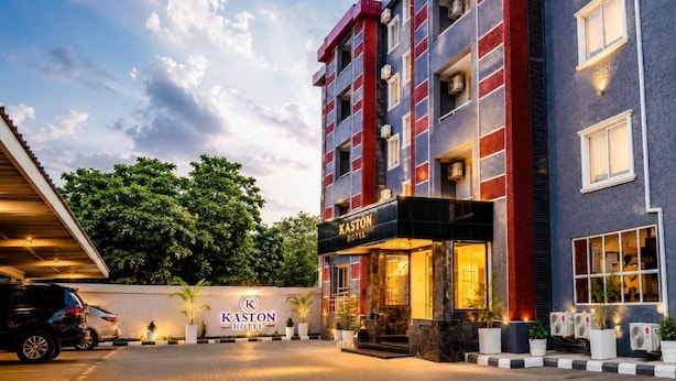 Um hotel com vários andares, entrada imponente, área de estacionamento e um jardim bem cuidado.
