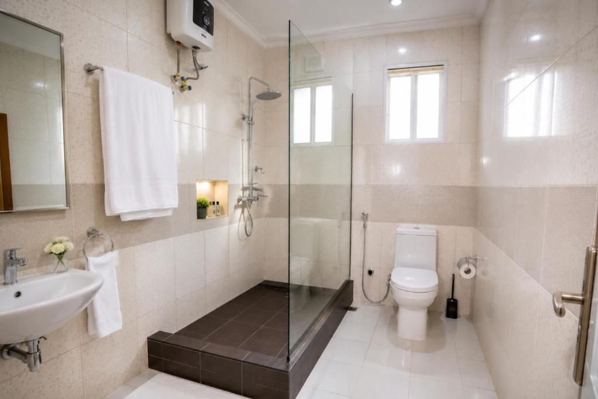 Un baño moderno con ducha envuelta en vidrio, un lavamanos blanco y un inodoro.