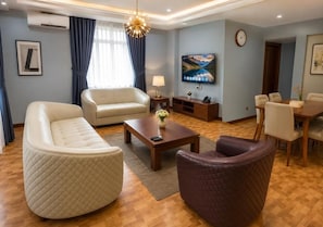 Una sala de estar moderna con sofá, sillón, mesa de centro y televisor montado en la pared.
