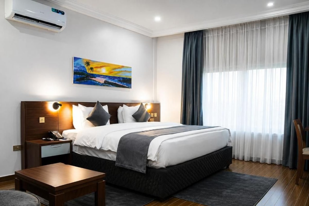 Une chambre d’hôtel avec un lit, des tables de chevet, un bureau et un tableau au mur.