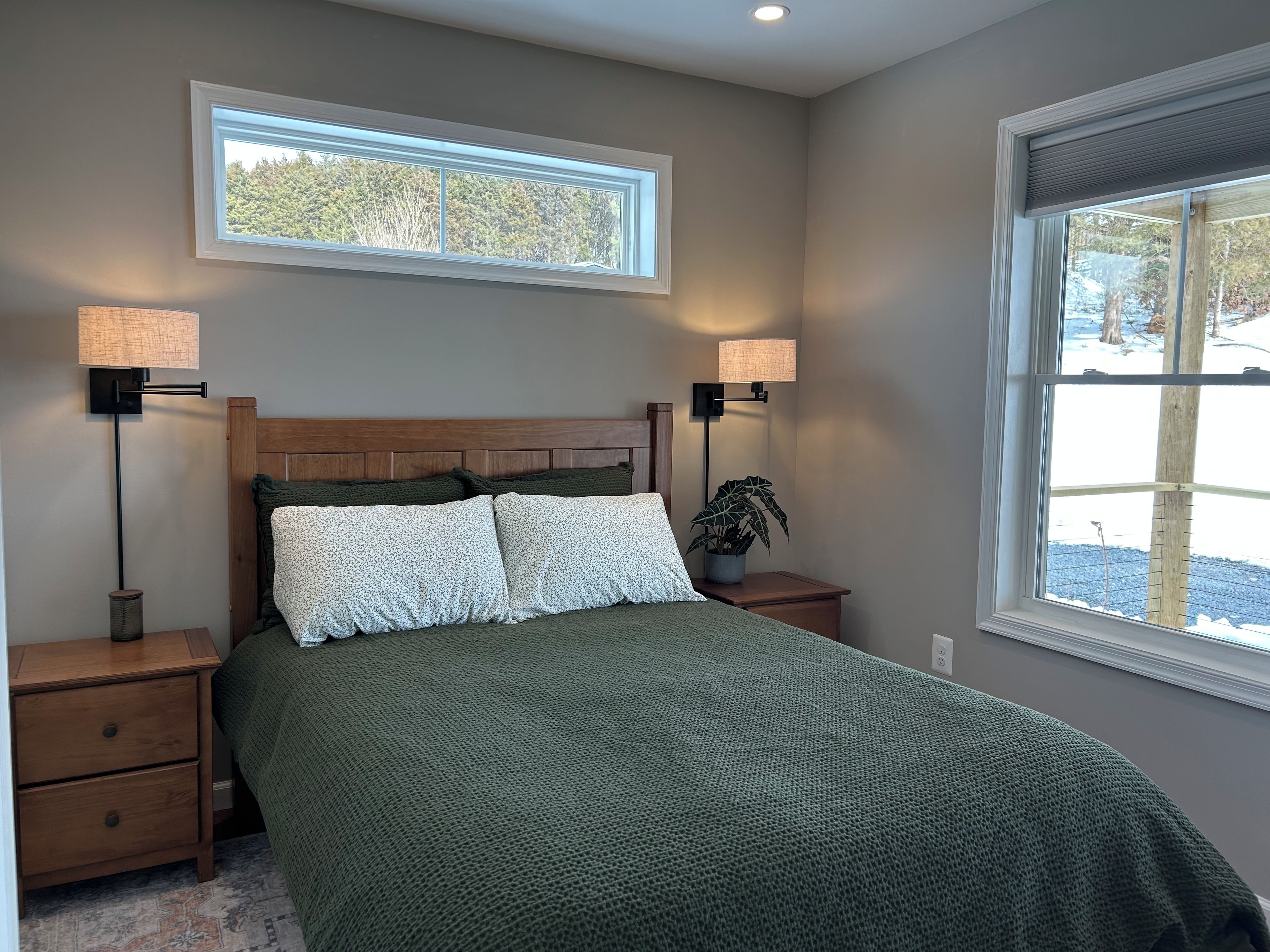 A bedroom with a bed, two bedside lamps, a nightstand, a window, and a potted plant.