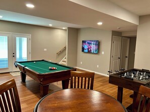 A room with a pool table, a foosball table, a television mounted on the wall, and a staircase leading to another level. - Mountain Glory - New Modern Cabin with Hot Tub and Mountain Views (Rileyville)