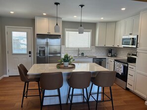 A modern kitchen with a central island, bar stools, stainless steel appliances, and white cabinetry. - Mountain Glory - New Modern Cabin with Hot Tub and Mountain Views (Rileyville)