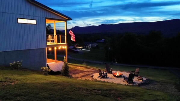 A building with a covered porch and a fire pit area. - Mountain Glory - New Modern Cabin with Hot Tub and Mountain Views (Rileyville)