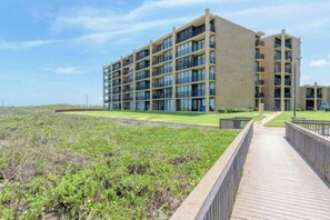 A multi-story building with a flat roof, large windows, and a paved walkway leading to it. - Apartment on South Padre Island (South Padre Island)