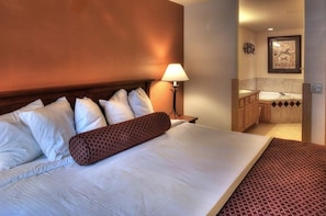 Une chambre d’hôtel avec un grand lit, une table de chevet, une lampe et une salle de bain visible à travers une porte ouverte.